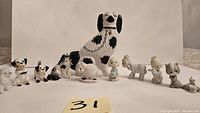 Front view of all 11 porcelain dog and animal figurines arranged in a row on a white surface.