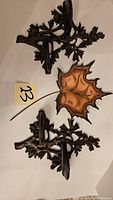 Three pieces laid flat: two dark wood tree branch wall hangers and one metal maple leaf wall hanger.