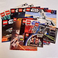 Photo showing a grouped layout of twelve LEGO Star Wars instruction booklets featuring different set numbers and Star Wars themed LEGO vehicles and characters on covers.