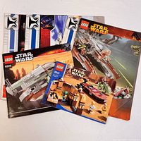 Nine LEGO Star Wars instruction booklets, including sets 6209, 7260, 4501, and 7675, laid out on a white surface. Covers show ship models and minifigures.