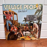 Front cover of Village People 'Go West' vinyl album showing band members in costumes outside with palm trees and truck in background