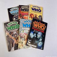 Diverse vintage Doctor Who paperback books and programme guide booklet arranged on flat surface showing front covers.