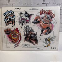 Front view of laminated vintage tattoo flash art sheet with various colorful tattoo character drawings and text "BAD BOY" and "HOG WILD".