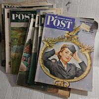 Stack of nine 1950s The Saturday Evening Post magazines showing various illustrated covers including a female service member on a winter-themed cover.