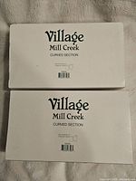 Two white boxes labeled 'Village Mill Creek Curved Section' stacked, showing product name and barcode.