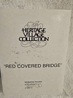 Close-up photo of Dept 56 Heritage Village Collection pamphlet/card showing the title 'Red Covered Bridge' and model number 5987-0 confirming item authenticity and brand.