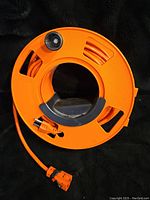Orange plastic reel holding orange extension cord with black handle and circular design.
