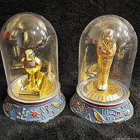 Two golden Egyptian figurines under clear domes on decorative blue bases with hieroglyphics.