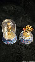 Two Franklin Mint Egyptian-themed figurines, one under glass dome, one with a globe missing, both on blue hieroglyphic bases with gold and red detailing.
