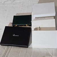 Several wallet boxes including one black Camelleon box and three white boxes on cardboard surface.