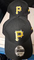 Front view of two black Pittsburgh Pirates caps with yellow 'P' logo, showing New Era 9FORTY adjustable model sticker on brim.