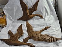 Top-down photo of three brown Syroco bird wallhangings arranged on white cloth background, showing detailed feather design and varying sizes.