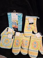 Overview of all items showing tablecloth packaging and three oven mitts/pot holders with tags