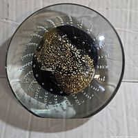 Top view of clear spherical glass paperweight revealing gold metallic textured core and radiating air bubble pattern around it.