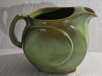 Front side view of green glazed ceramic pitcher with handle and spout