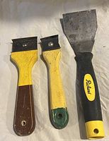 Three metal scrapers with different sized blades and worn handles.