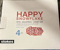 Photo of the box for a set of four Stokes Happy Snowflake glass plates, showing brand, product name, item count, and embossed snowflake design on the box.