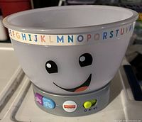 White children's toy bowl with smiling face and alphabet letters around rim, gray base with buttons and Fisher-Price logo