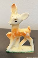 Front view of vintage fawn-shaped candle showing orange and white coloration with black eyes on a green edged base.