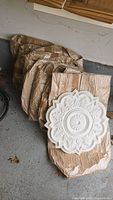 Eight individually wrapped round ornate plaster ceiling tiles stacked together with one tile visible, showing intricate floral and geometric relief design.