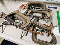 Photo of assorted metal adjustable C-Clamps on a white surface, showing varying sizes and use wear.