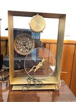 Brass-tone rectangular clock case with glass panels, electrical cord visible