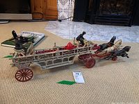 Side view of the vintage cast iron fire truck toy with three horses and two driver figures, showing details of the ladder and wheels.