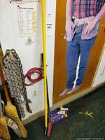 Full view of the lot including heavy chains hanging on wall, two handheld scraper tools with long yellow and red handles standing on floor, red coiled hose, and push broom.
