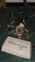 Photo showing multiple dust-covered handheld tools and the oval/circle mat cutter box on a green floor.