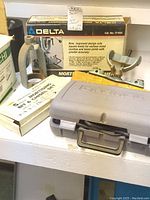 Photo showing Delta mortising attachment box, Eagle Tools mortising chisels and bits set in original packaging, and gray Dremel Multi-Pro tool case on a shelf.