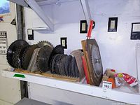 Photo of multiple circular saw blades organized on a wooden shelf in a workshop environment.