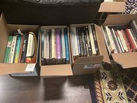 Four boxes filled with books stacked inside, visible titles on top layers showing various horology and art subjects