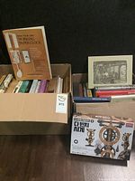 Photo of two boxes containing assorted books, a paper clock kit box, and framed artwork.