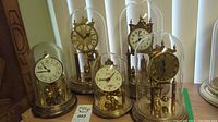 Group shot of five anniversary clocks under glass domes on varying metal bases