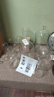 Several glass domes arranged on a carpeted floor, different sizes and shapes, some domes contain tags.