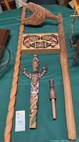 Overall assortment of carved wooden staffs, painted box and whistle on green tablecloth