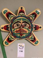 Full front view of the Indigenous art sun-shaped wooden clock with vibrant painted face and strong facial details.