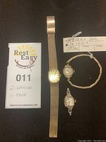 Three watch items on black background including gold-tone mesh bracelet watch, small round Rolex Precision watch, square Caravelle watch face