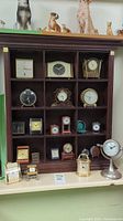 Wooden display case holding 13 small tabletop clocks in various styles