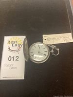 Silver pocket watch with English hallmarked tag, and Rest Easy Removals lot number tag indicating 'Pocket Watch'.