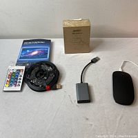 Lot contents showing USB LED TV backlight strip, Aukey webcam box, Bluetooth mouse and USB-C adapter on table.
