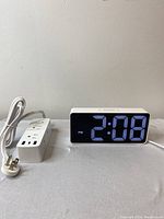 Digital alarm clock next to white power bar extension cord, clock displaying 2:08 PM