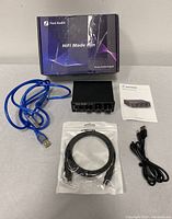 Fosi Audio DAC-Q4 DAC device with cables and box on grey surface.