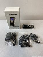 Image of the Jawploy digital voice recorder alongside its box and three sealed accessories: charger, headphones, and cables.