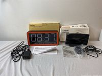 Both electronic devices including electric alarm clock and wireless LED digital timer with all accessories and boxes, displayed on table.