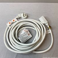 Coiled white electrical cord with polarized male plug and female connector with printed safety warnings attached.