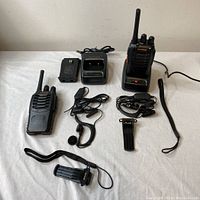 Set of two Baofeng FM transceivers each with antenna, earpieces, chargers, belt clip, and wrist strap displayed on a white surface