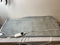 Full view of the large gray electric heating pad laid on a table, showing the textured quilted pattern of the pad.