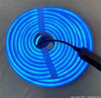 Coiled LED light strip powered on, glowing bright blue with black inline controller visible
