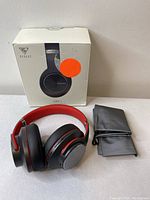 Headphones set arranged with original box behind and gray carrying pouch to the right, showing overall contents.